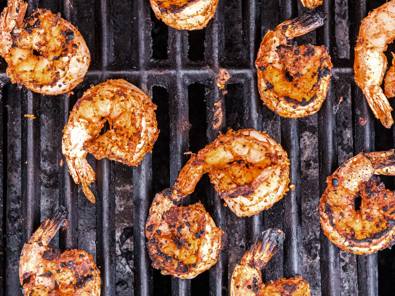 Shrimp developing charred grill marks as they cook, turning golden brown.