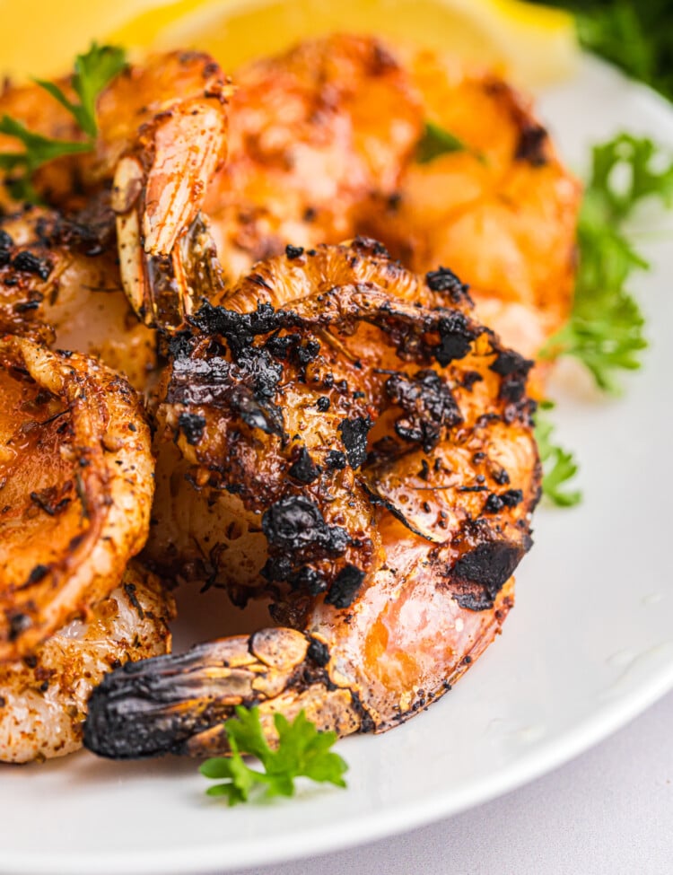 Juicy Cajun grilled shrimp with charred edges arranged on a plate, garnished with fresh parsley and lemon.