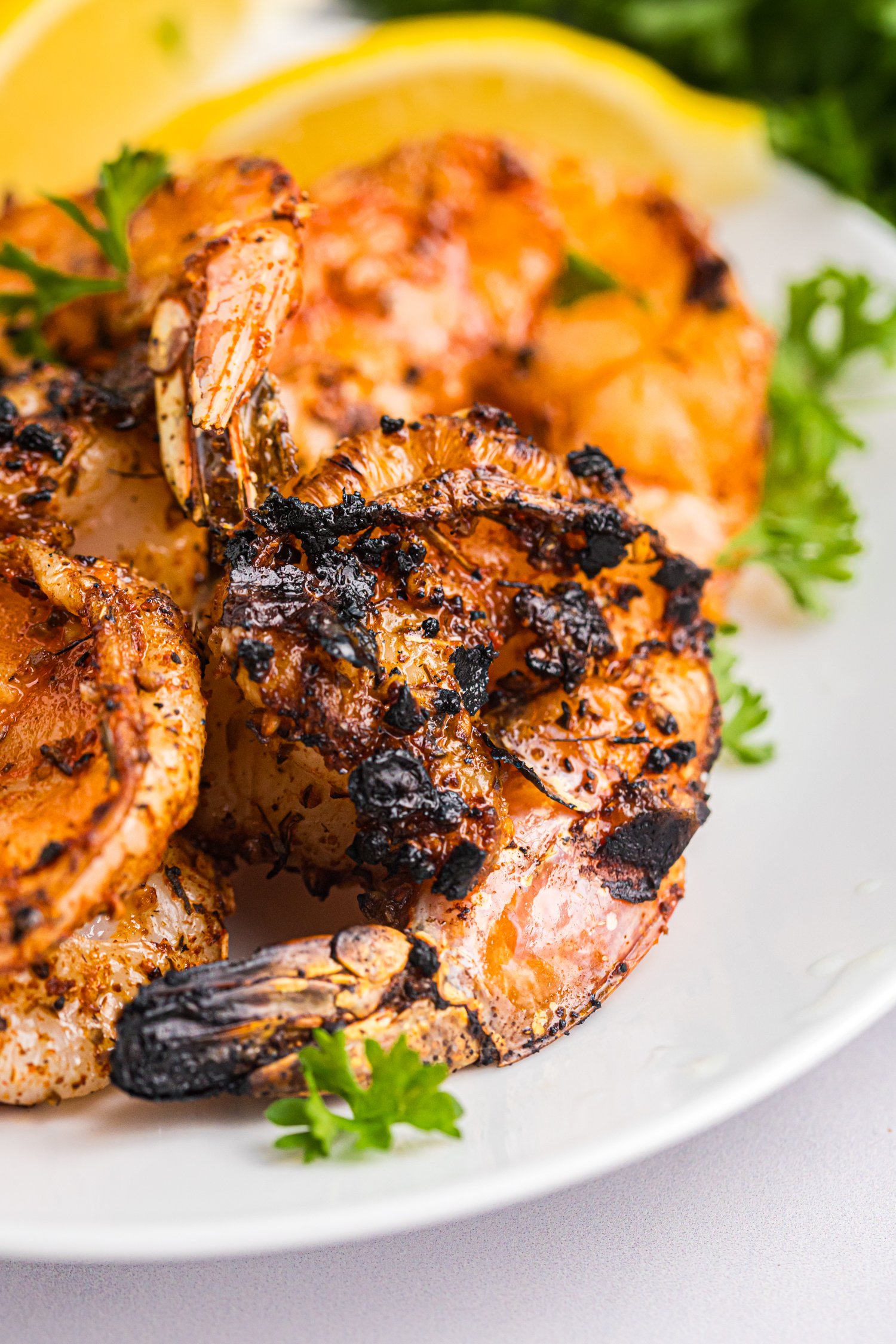 Juicy Cajun grilled shrimp with charred edges arranged on a plate, garnished with fresh parsley and lemon.