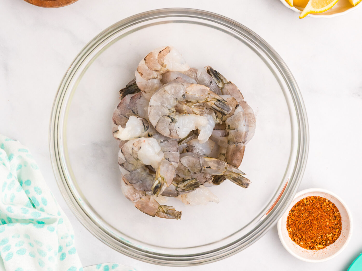 Raw shrimp placed in a clear glass bowl, ready for seasoning, with Cajun spice mix nearby.
