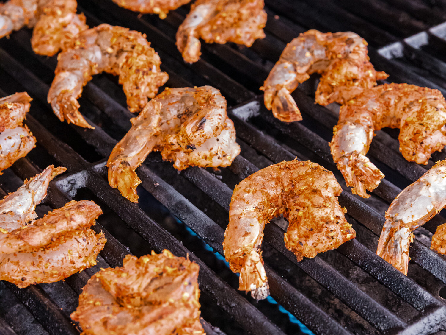 Seasoned shrimp placed directly on a grill with flames underneath, beginning to cook.