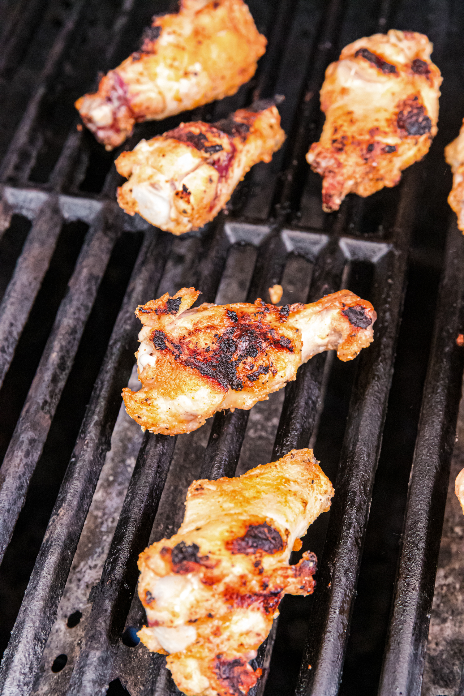 Close-up of chicken wings on a grill, charred and golden brown with crispy edges.