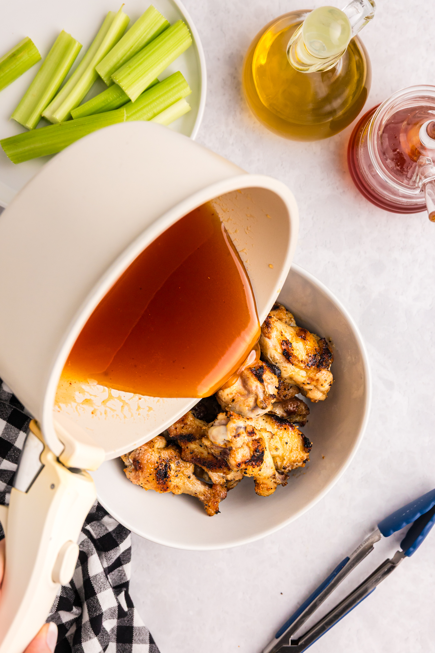 Hot honey sauce being poured from a saucepan over a bowl of freshly grilled chicken wings.