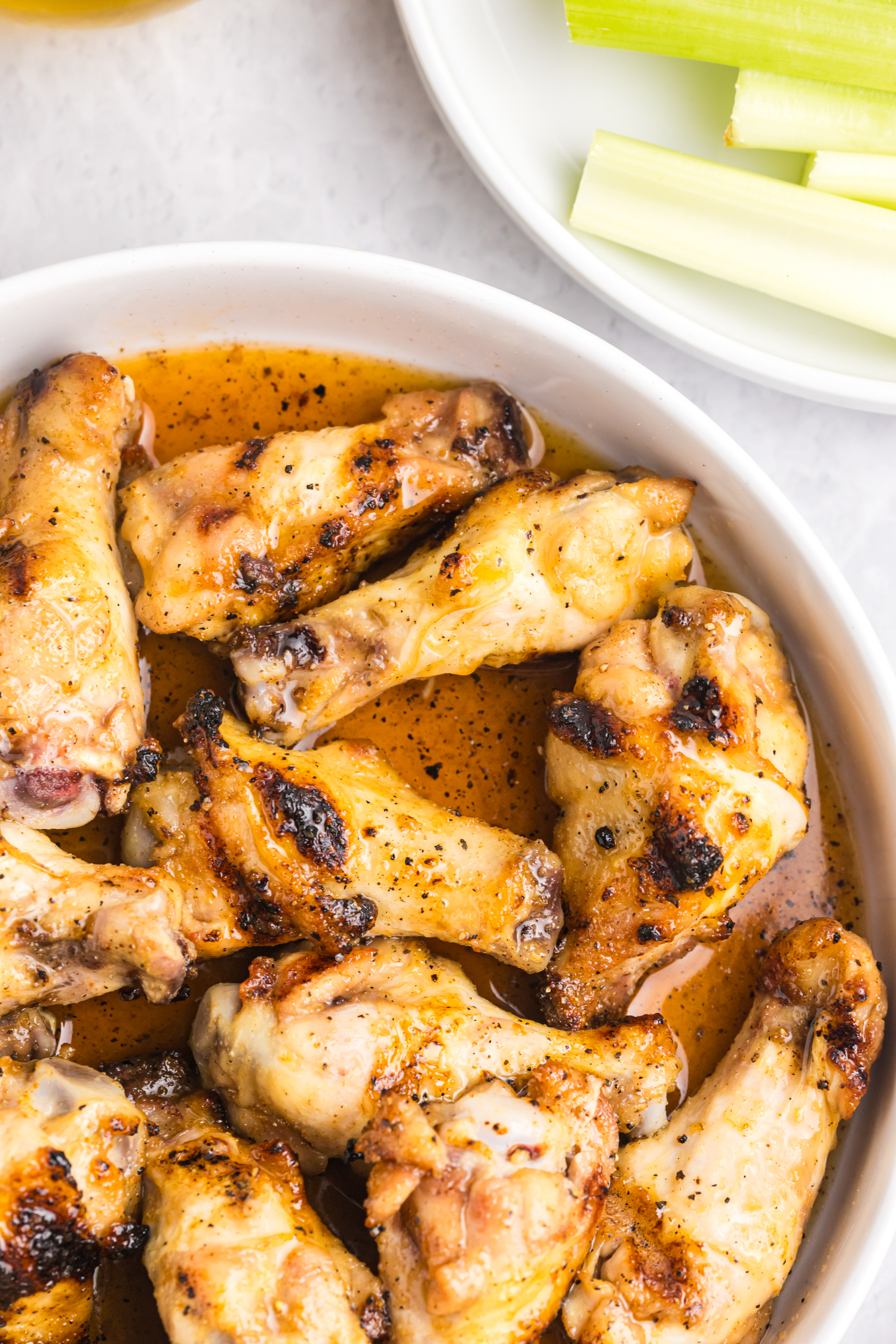 Close-up view of chicken wings glistening in hot honey sauce inside a white bowl.