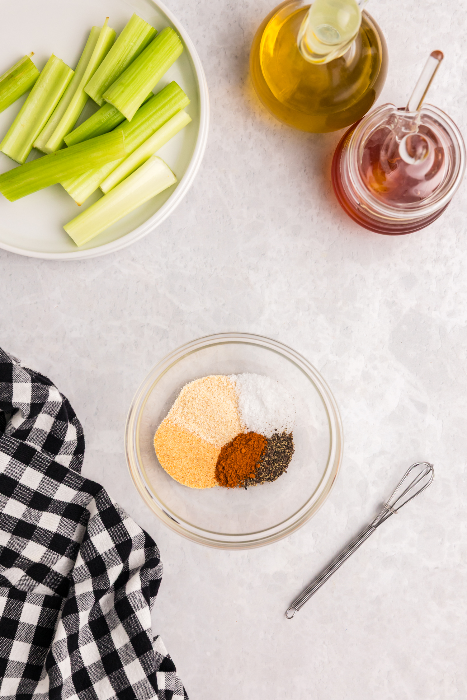 Ingredients for seasoning displayed: celery sticks, jars of oil and honey, and a small bowl with garlic powder, onion powder, paprika, salt, and pepper.