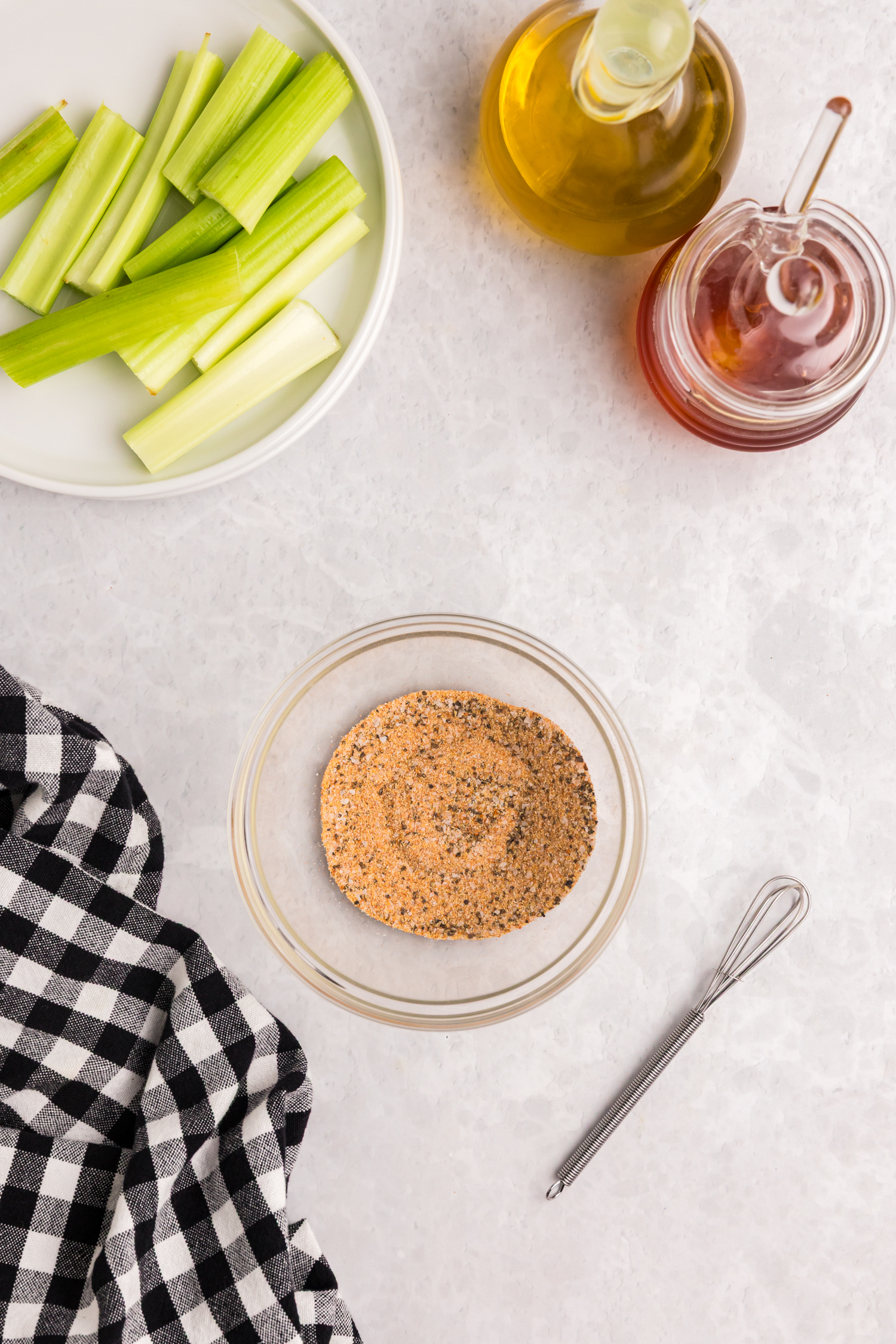 Seasoning spices mixed together in a glass bowl, surrounded by celery, oil, and honey.