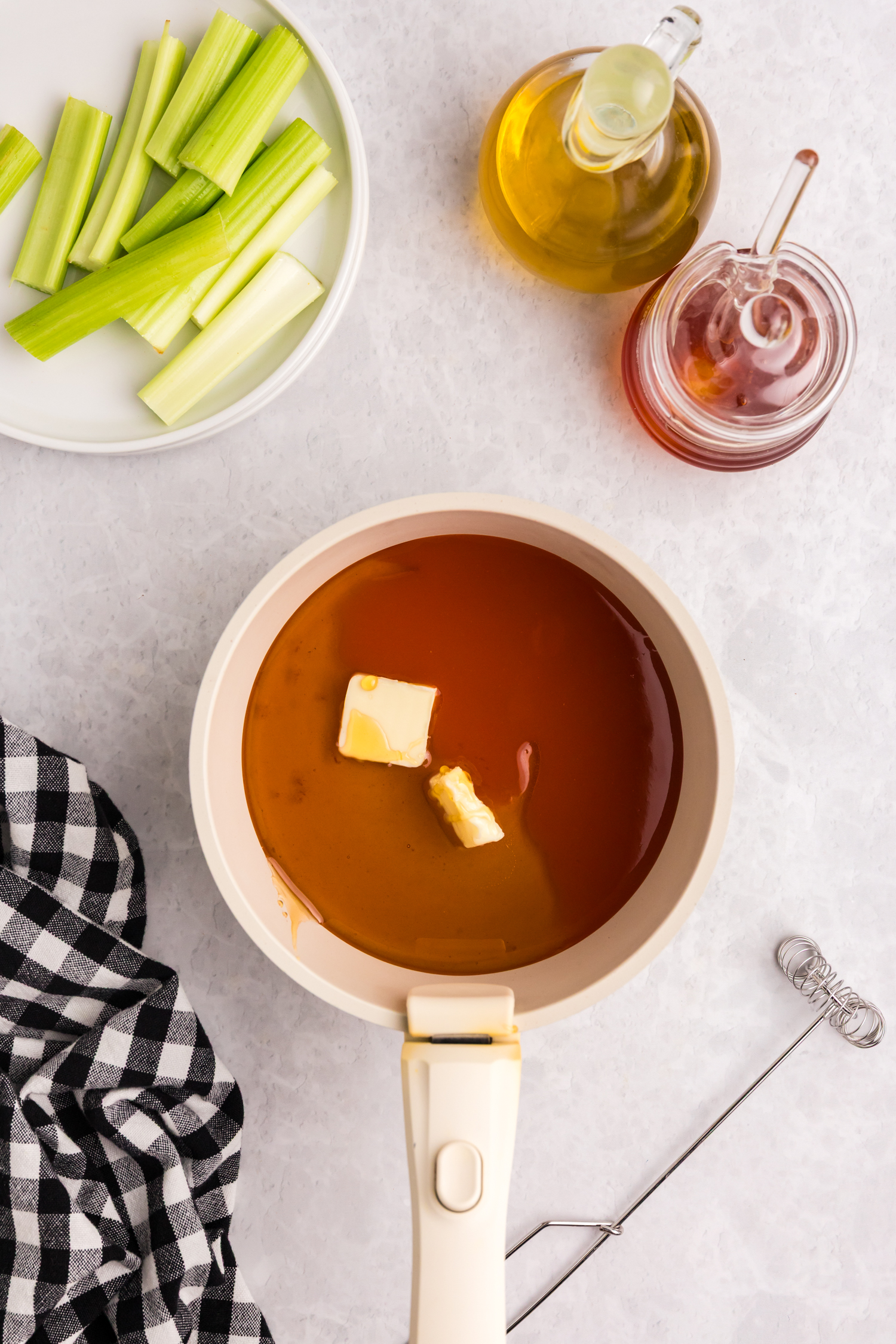 Sauce mixture of butter, hot sauce, and honey starting to melt in a saucepan.