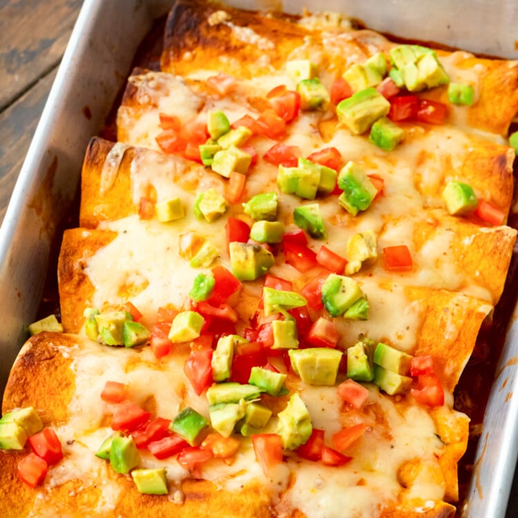 A pan of Pulled Pork Enchiladas topped with diced tomatoes and avocado