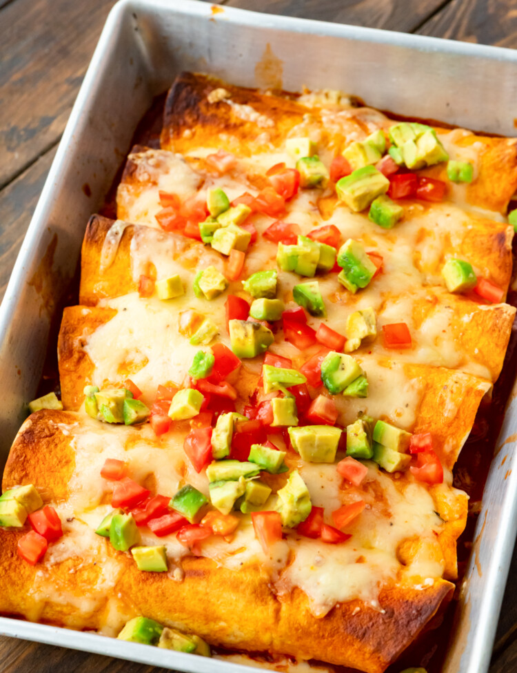 A pan of Pulled Pork Enchiladas topped with diced tomatoes and avocado