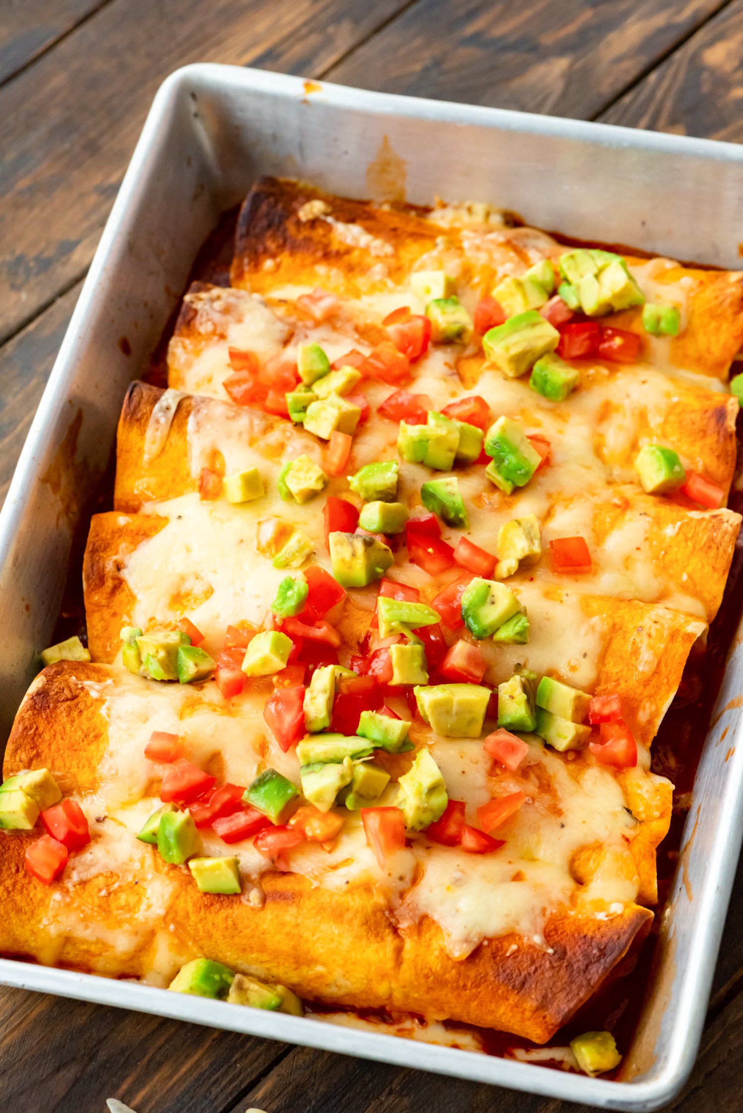 A pan of Pulled Pork Enchiladas topped with diced tomatoes and avocado