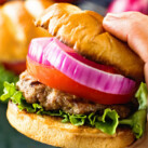 Hand holding a grilled burger with toppings