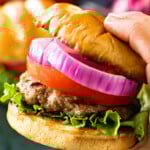 Hand holding a grilled burger with toppings