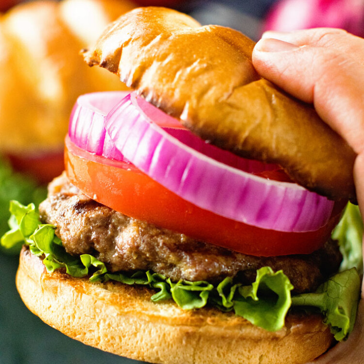 Hand holding a grilled burger with toppings