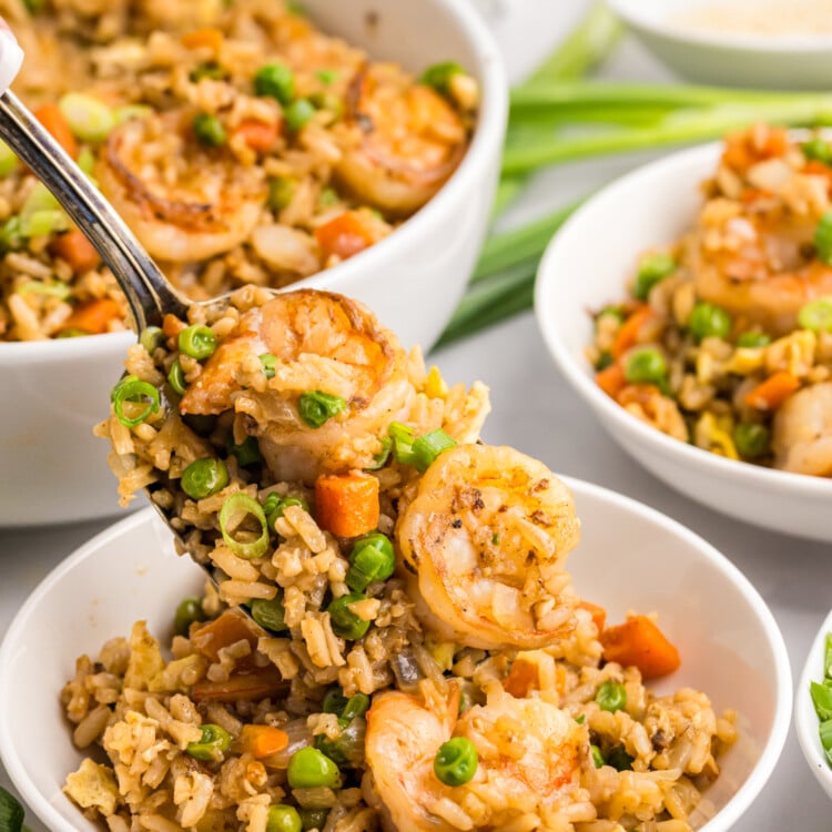 A spoonful of shrimp fried rice with peas, carrots, and green onions held above a bowl.