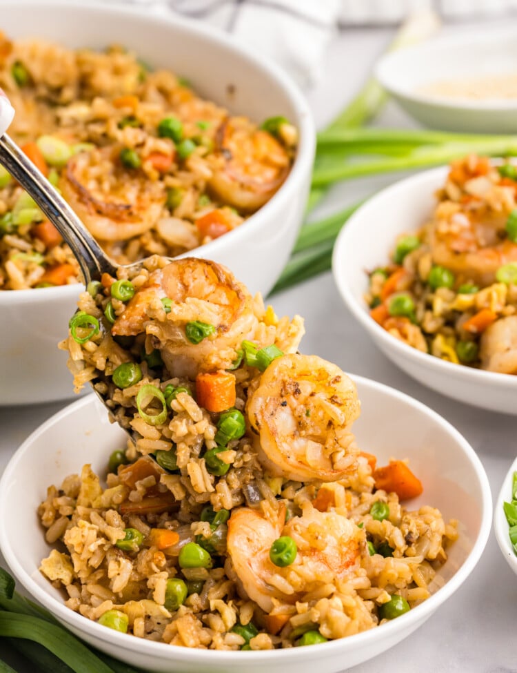 A spoonful of shrimp fried rice with peas, carrots, and green onions held above a bowl.