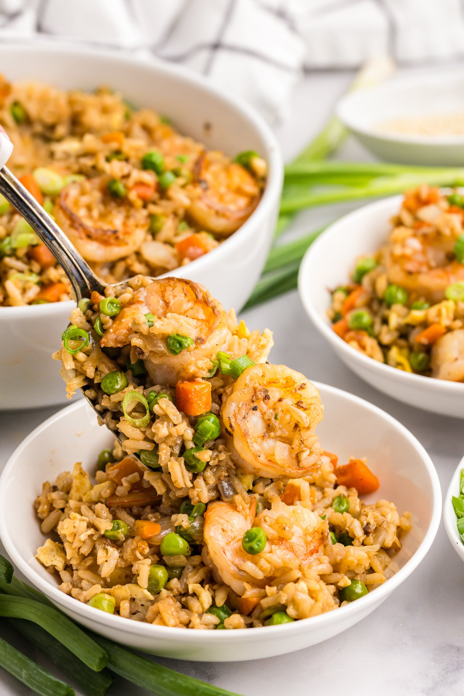 A spoonful of shrimp fried rice with peas, carrots, and green onions held above a bowl.