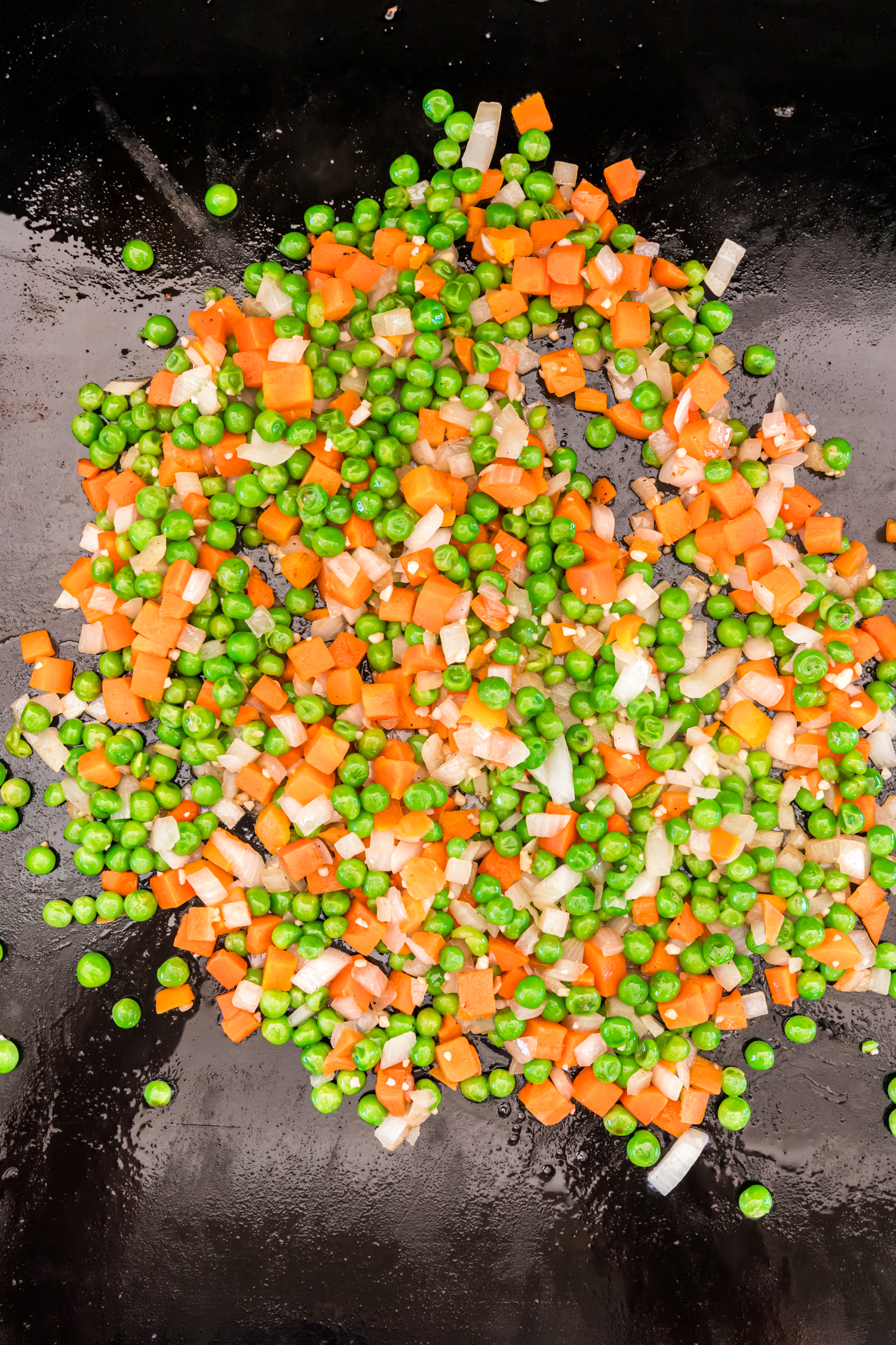 Diced carrots, peas, onions, and garlic being sautéed on a griddle.