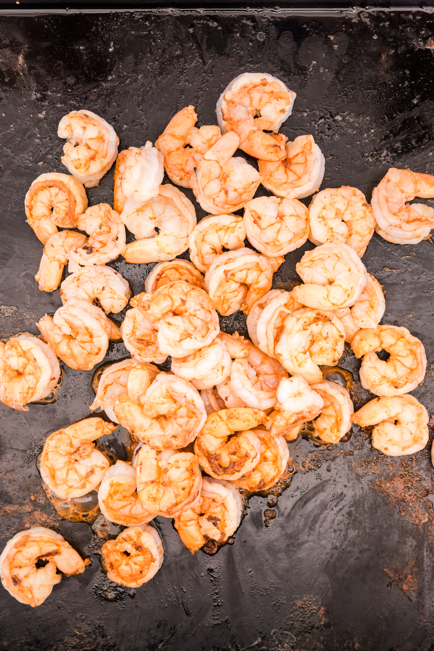 Shrimp being cooked on a hot griddle until pink and slightly browned.