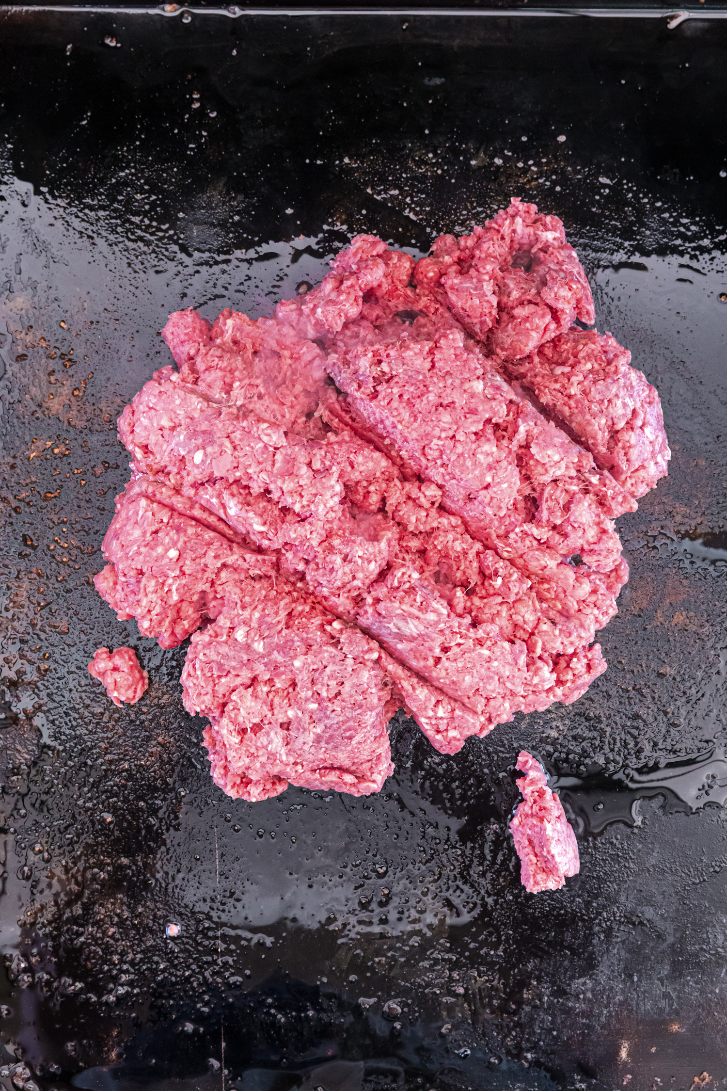 A soft taco filled with ground beef, shredded lettuce, diced tomatoes, and shredded cheese on a white plate, surrounded by bowls of taco toppings including black olives, salsa, and sour cream.