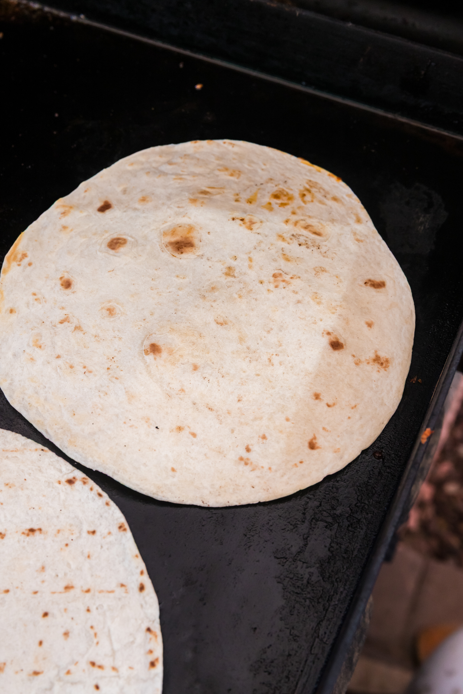 Partially cooked ground beef on a griddle topped with taco seasoning and salsa, ready to be mixed together.