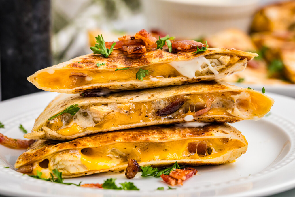 Close-up of stacked bacon chicken ranch quesadilla slices filled with melted cheese, chicken, bacon, and ranch sauce.