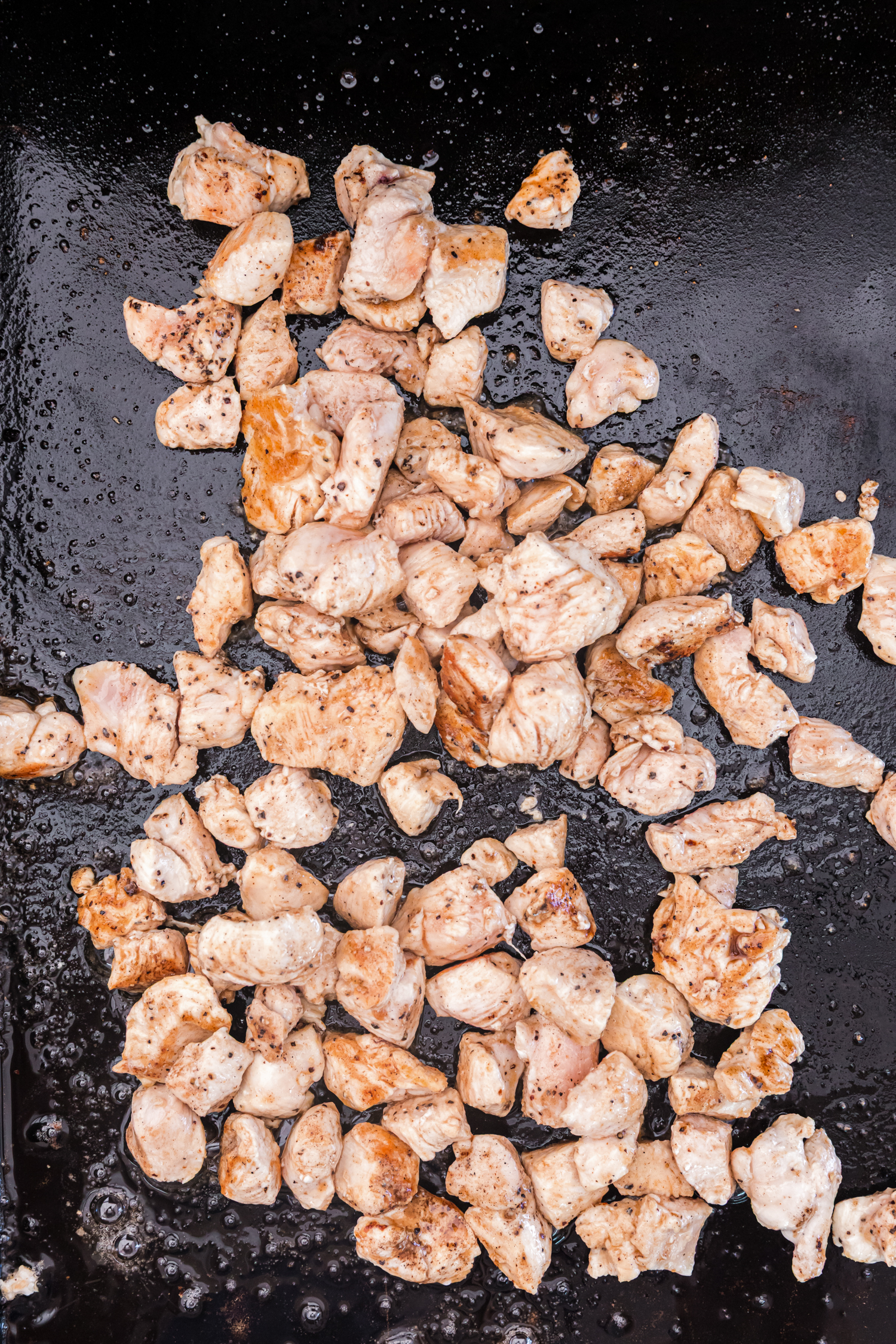 Chicken pieces browning on a griddle, cooked until golden and tender.