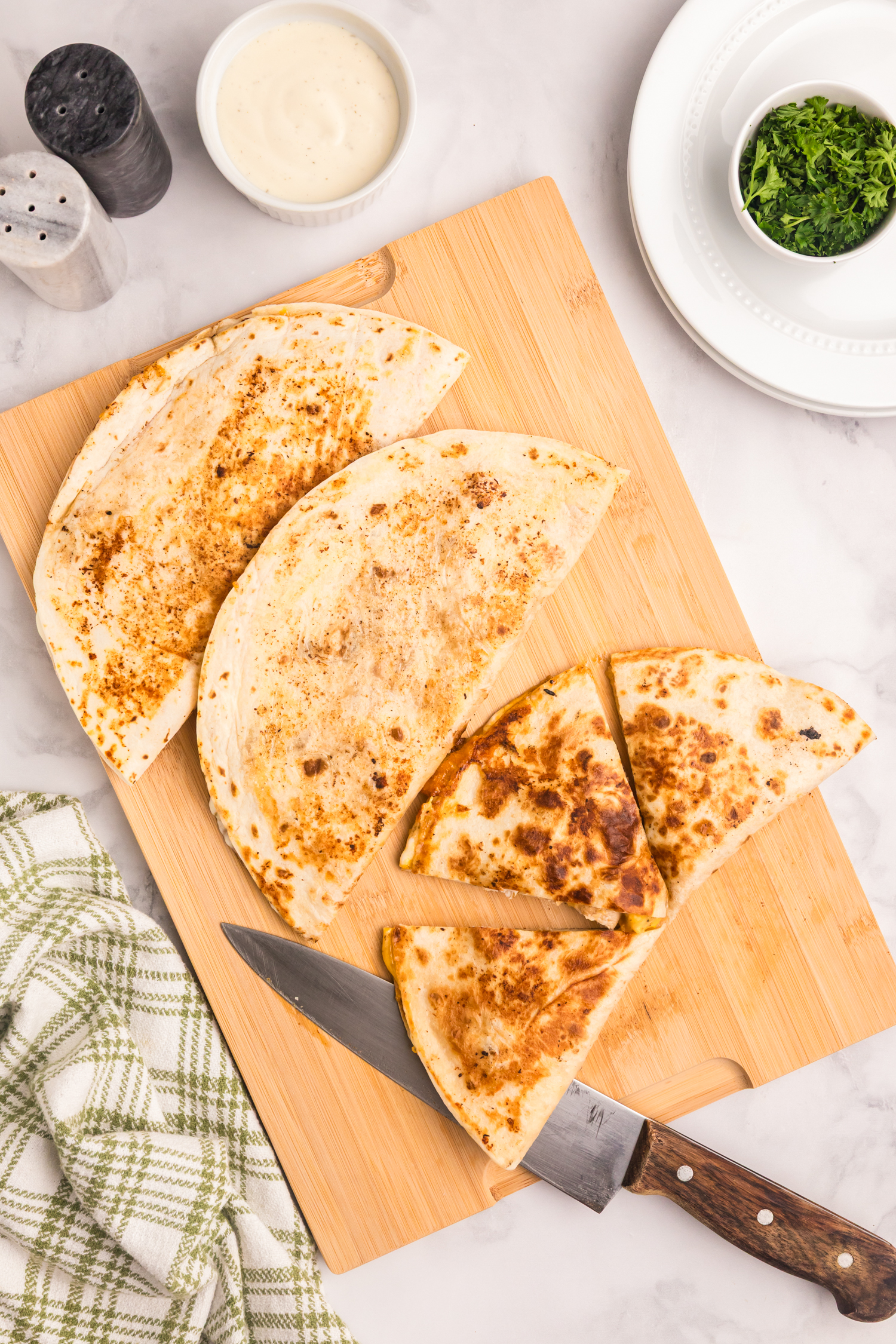 Golden brown quesadillas on a cutting board, some sliced into triangles with a knife beside them.