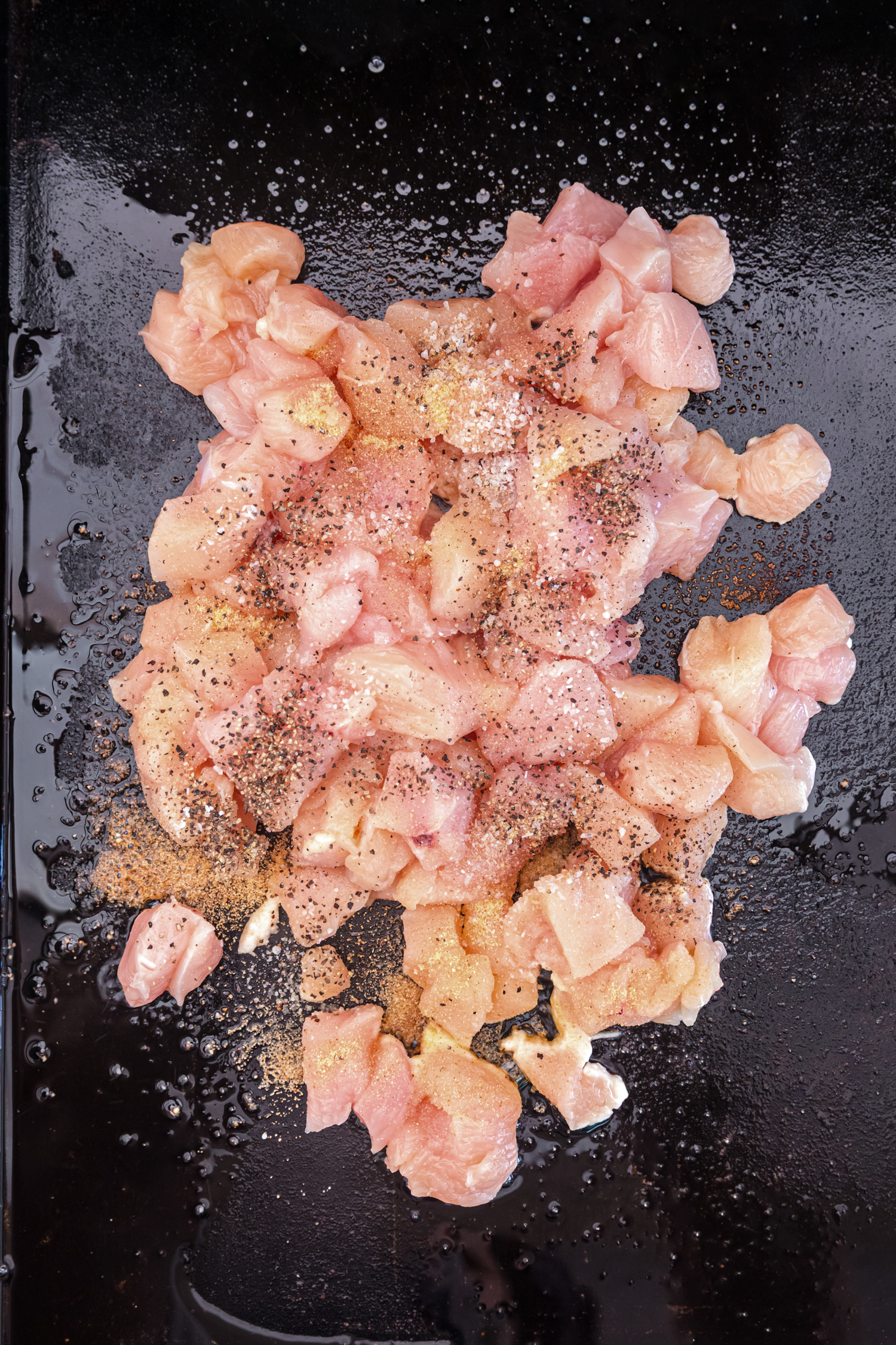 Raw diced chicken seasoned with salt, pepper, and spices cooking on a hot griddle.