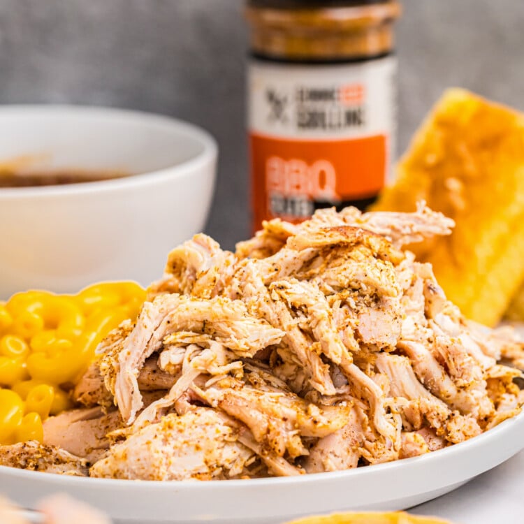 Close-up of shredded smoked chicken in a white dish with side dishes in the background.