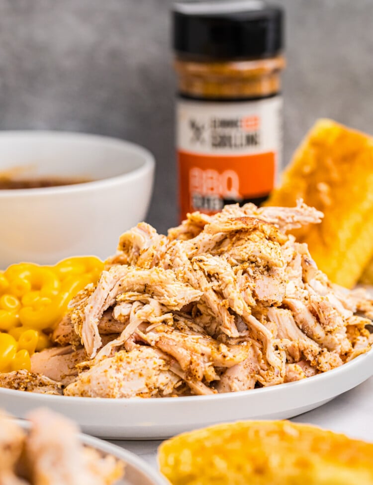 Close-up of shredded smoked chicken in a white dish with side dishes in the background.