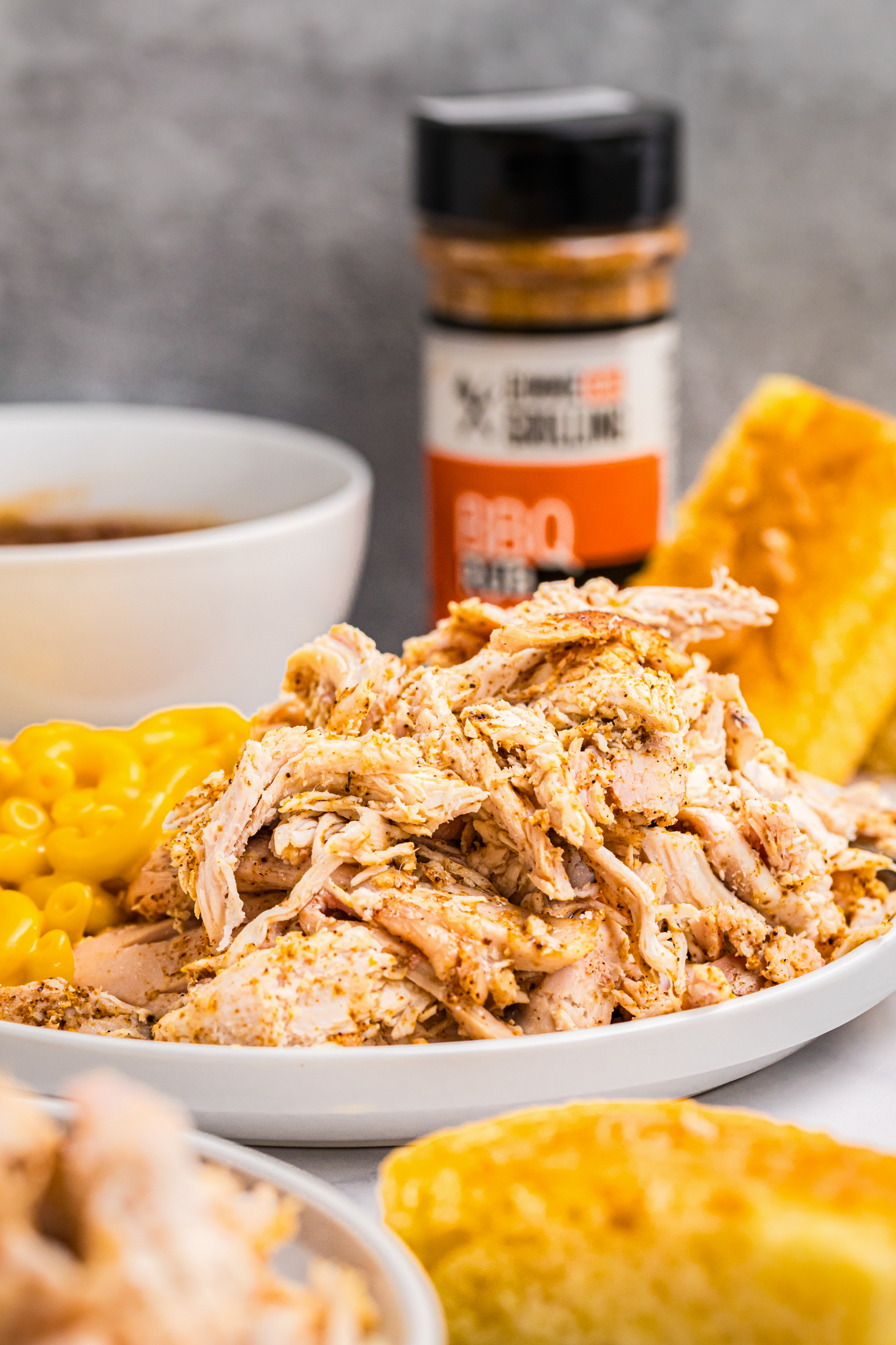 Close-up of shredded smoked chicken in a white dish with side dishes in the background.