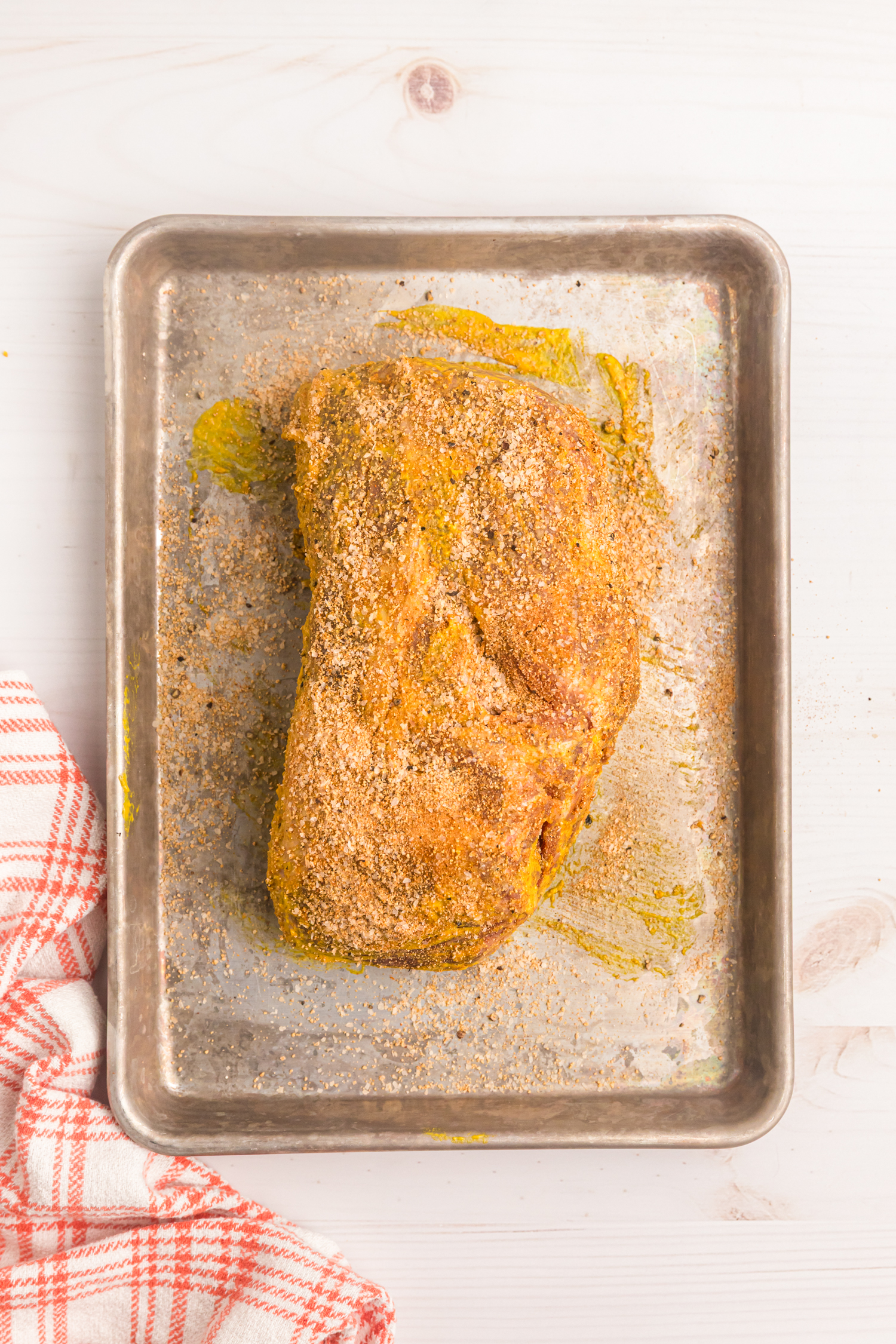 Raw chuck roast coated in mustard and dry rub seasoning on a metal baking sheet, ready to go into the smoker.