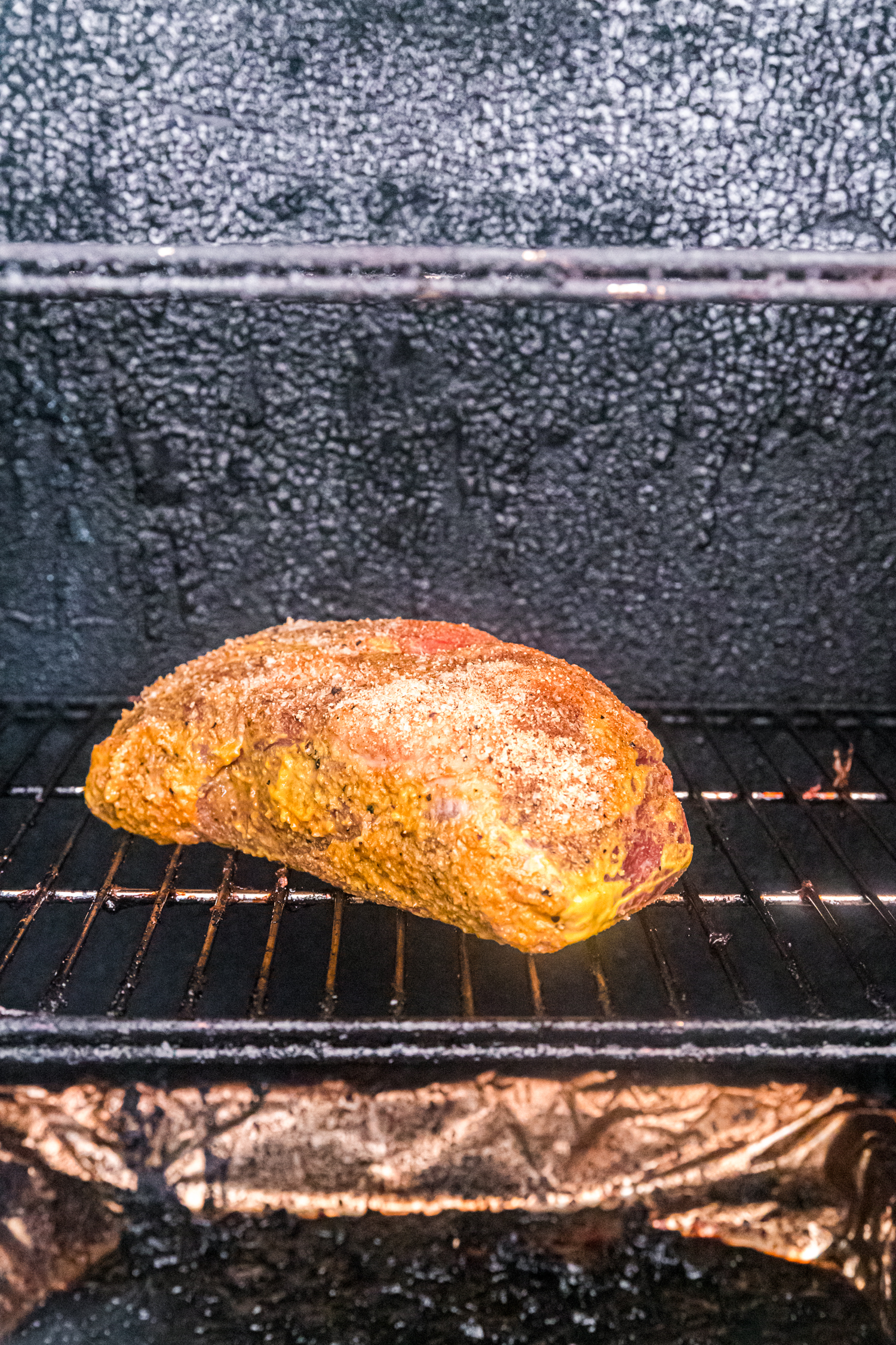 Seasoned chuck roast sitting on the grate inside a smoker, beginning the smoking process.