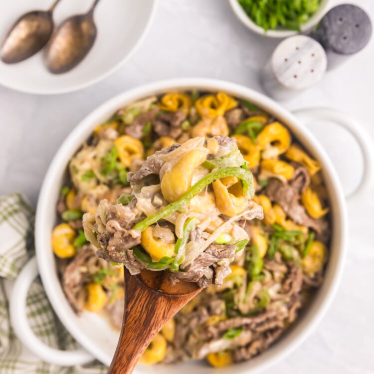 A spoonful of cheesy Philly cheesesteak tortellini being lifted from a serving dish.