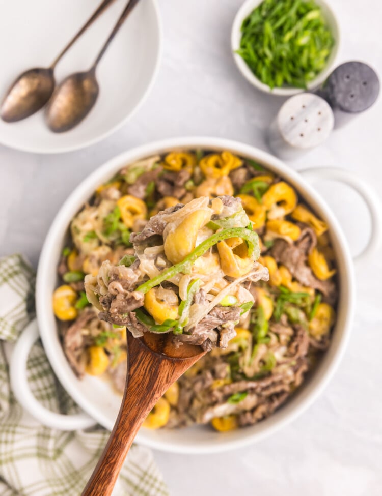 A spoonful of cheesy Philly cheesesteak tortellini being lifted from a serving dish.