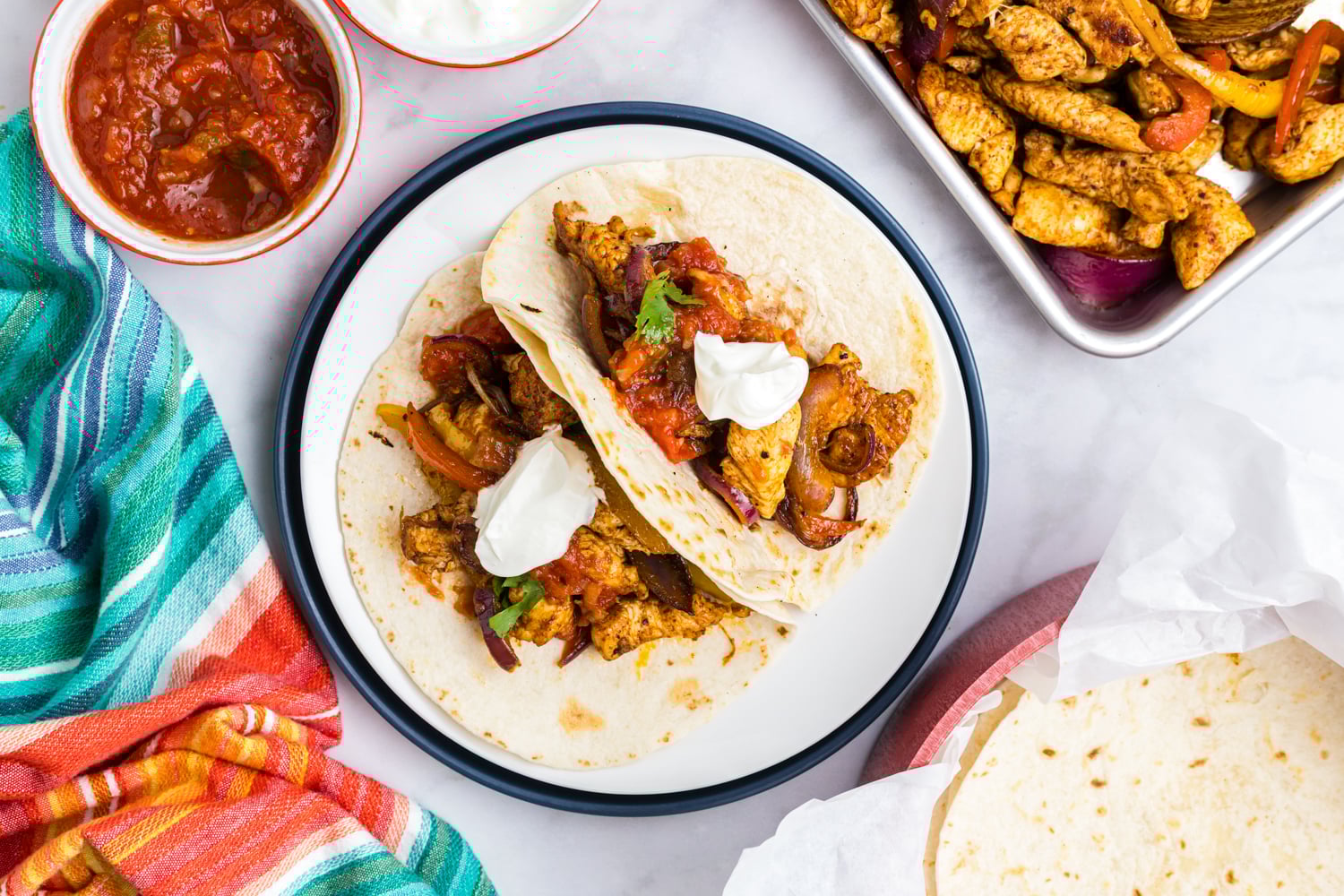 Chicken fajitas assembled in flour tortillas and topped with salsa and sour cream on a plate.