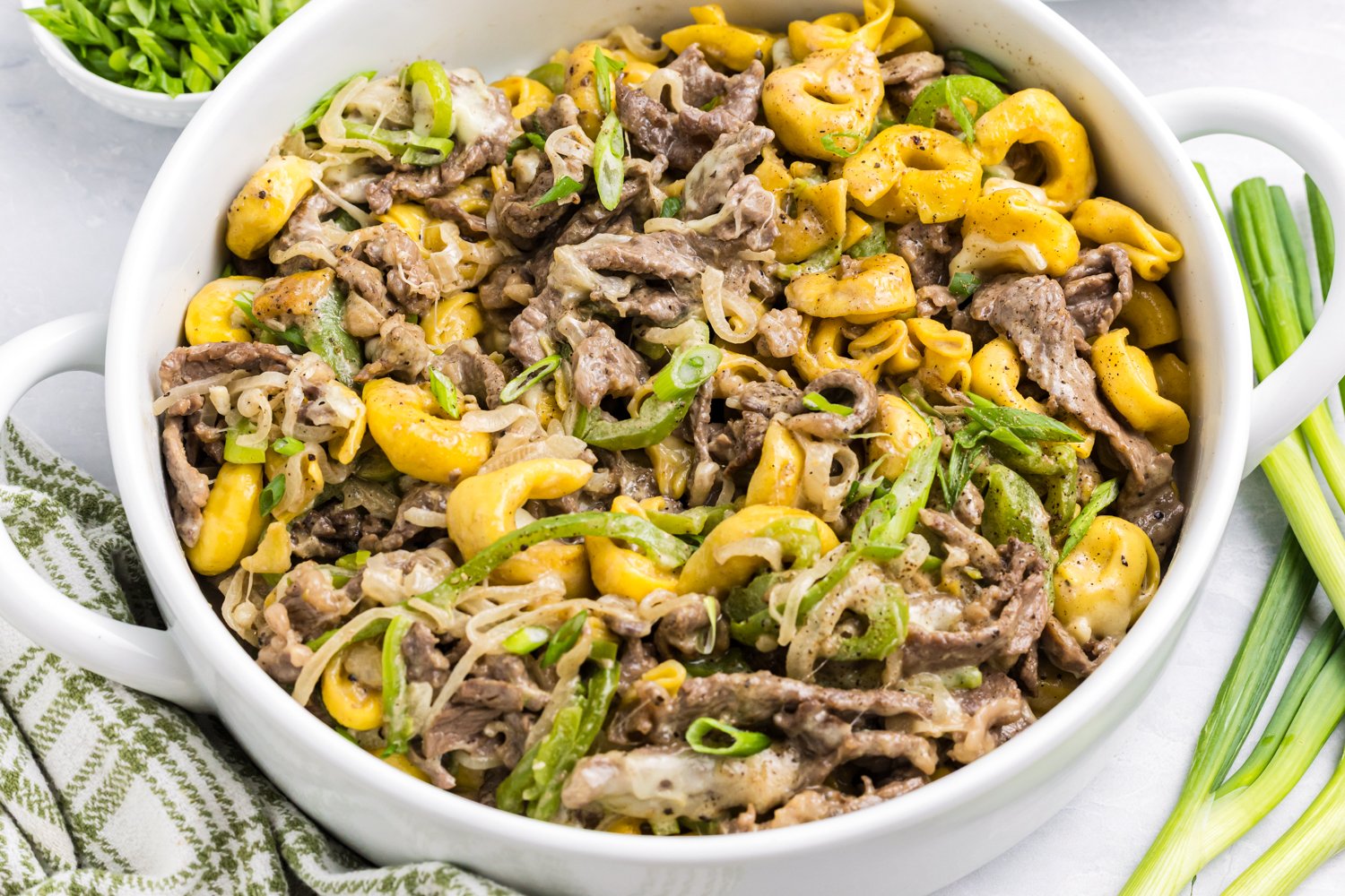Two bowls of Philly cheesesteak tortellini garnished with sliced green onions, ready to serve.