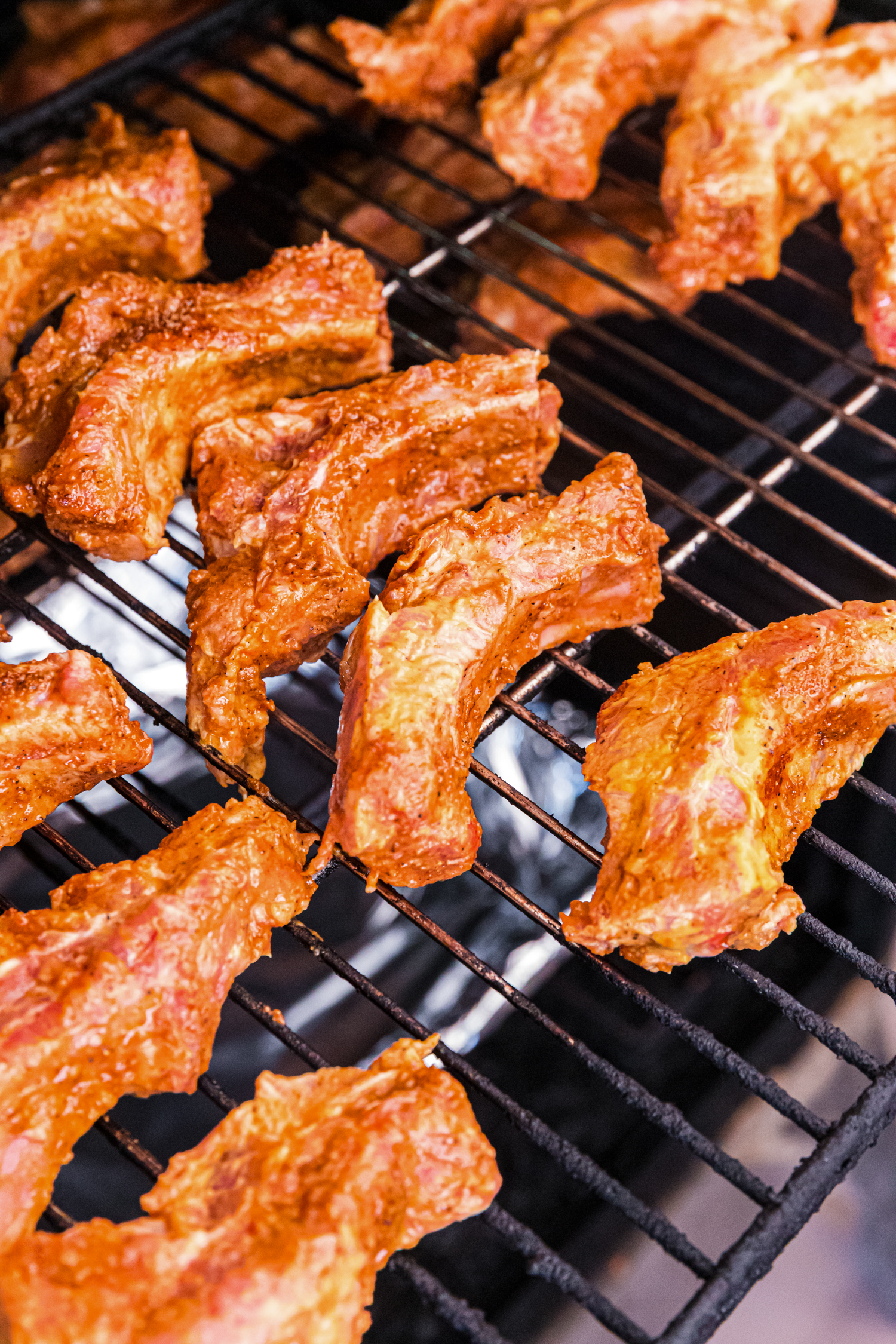 Seasoned pork ribs cooking on a grill grate, lightly browned and spaced apart over indirect heat.
