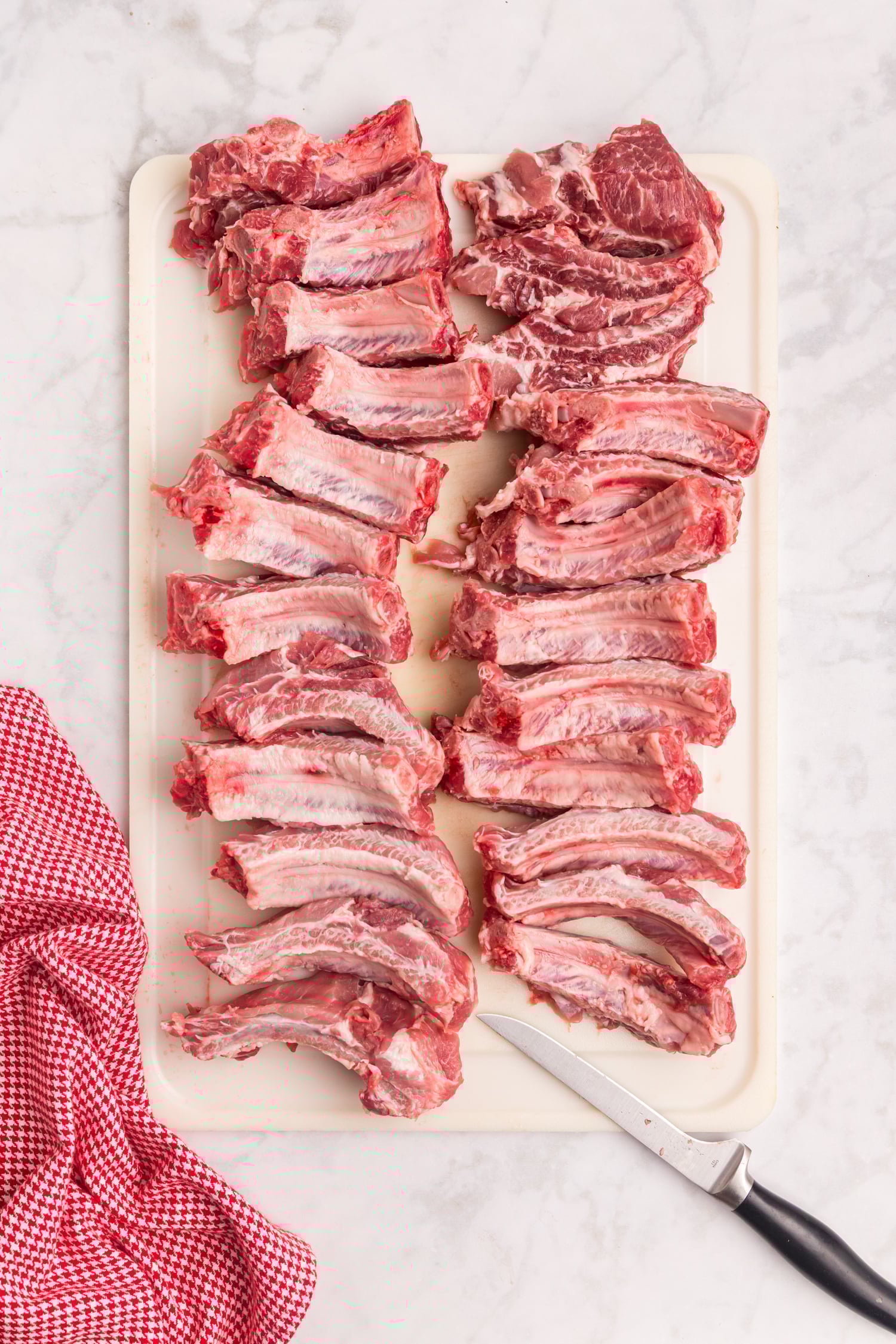 Raw pork ribs cut into individual portions arranged on a white cutting board with a knife beside them.