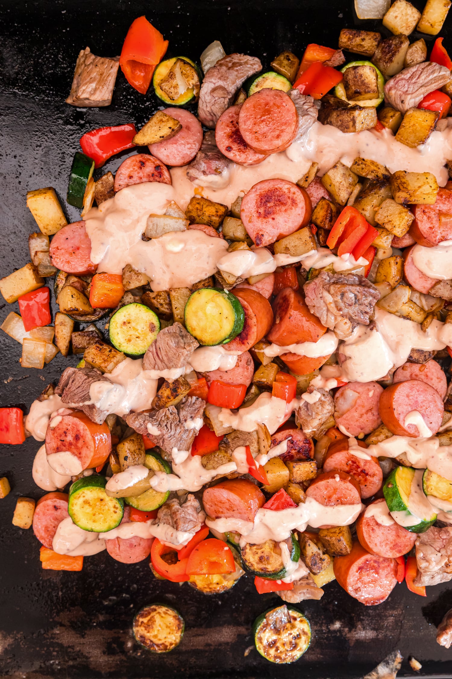 Griddle stir-fry of sausage, beef, potatoes, zucchini, peppers, and onions drizzled with a creamy sauce.