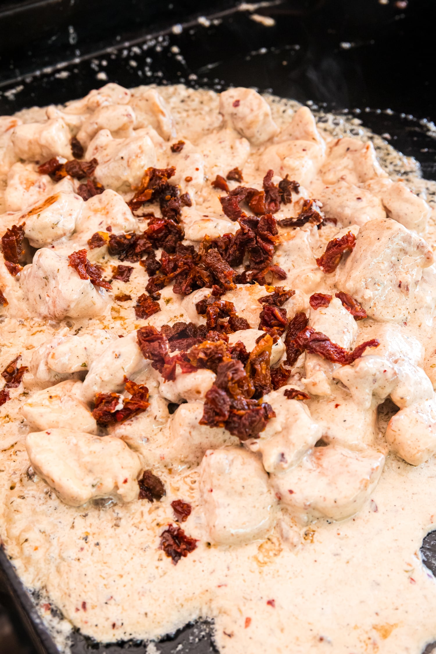 Chicken simmers in a creamy sauce on the griddle, topped with chopped sun-dried tomatoes as the sauce thickens and bubbles.