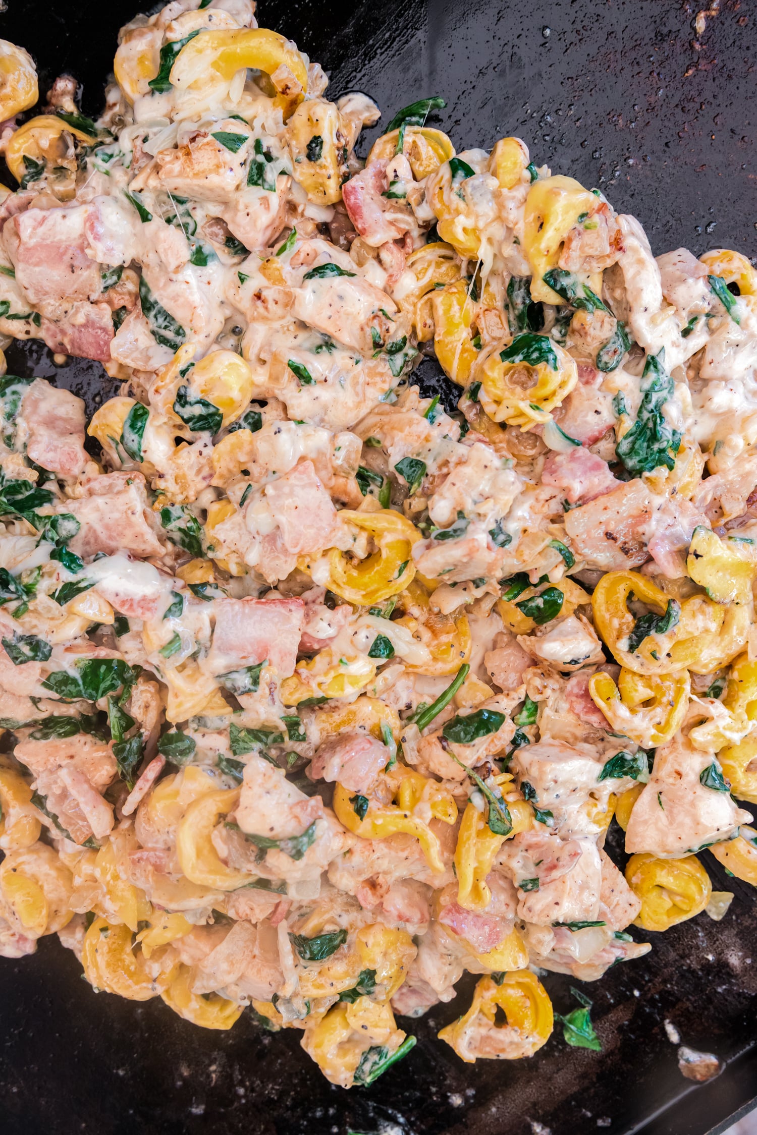 Chicken bacon ranch tortellini mixture cooking on a griddle with melted creamy sauce and spinach.