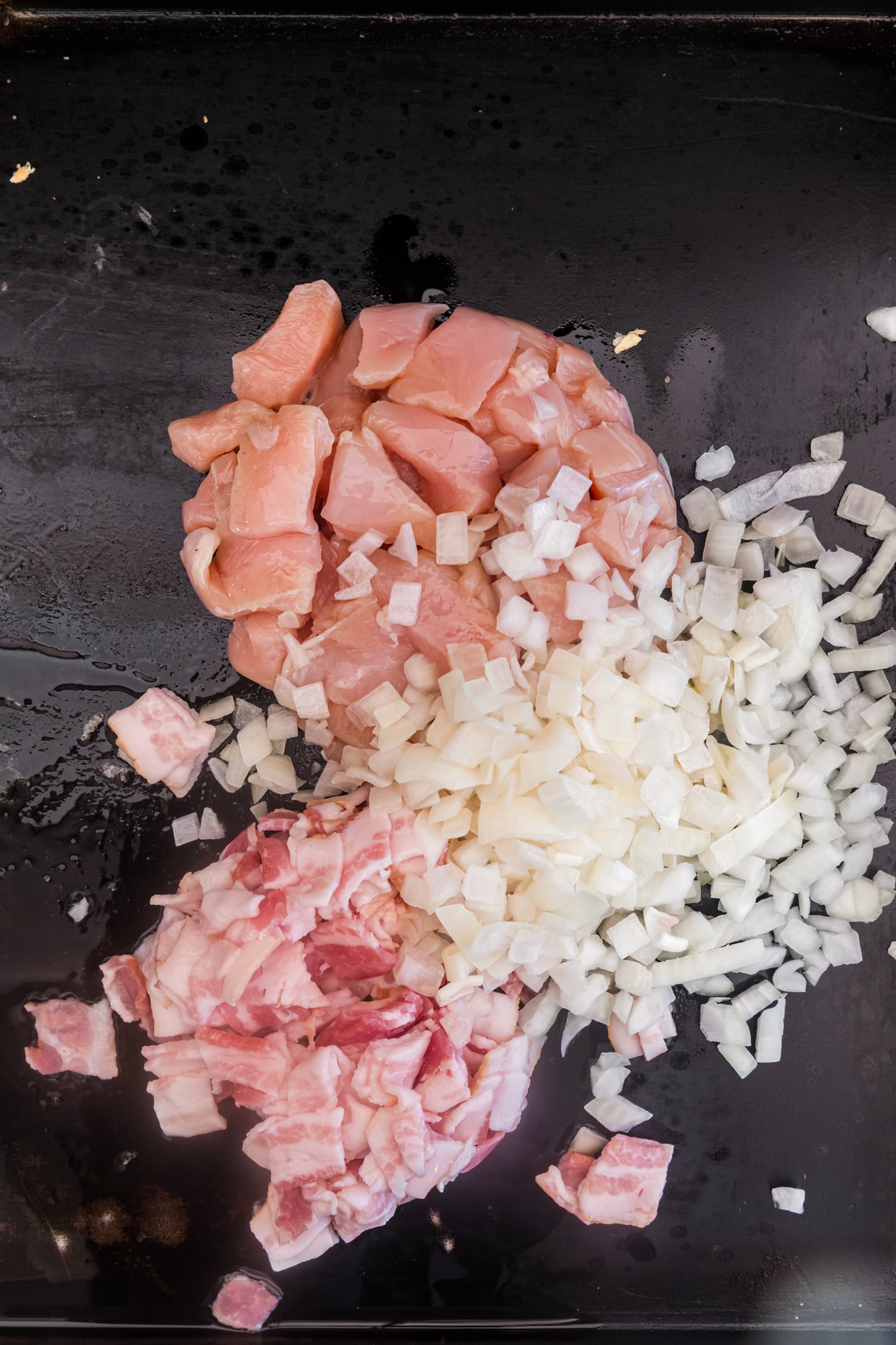 Diced chicken, chopped bacon, and diced onions cooking together on a flat-top griddle.