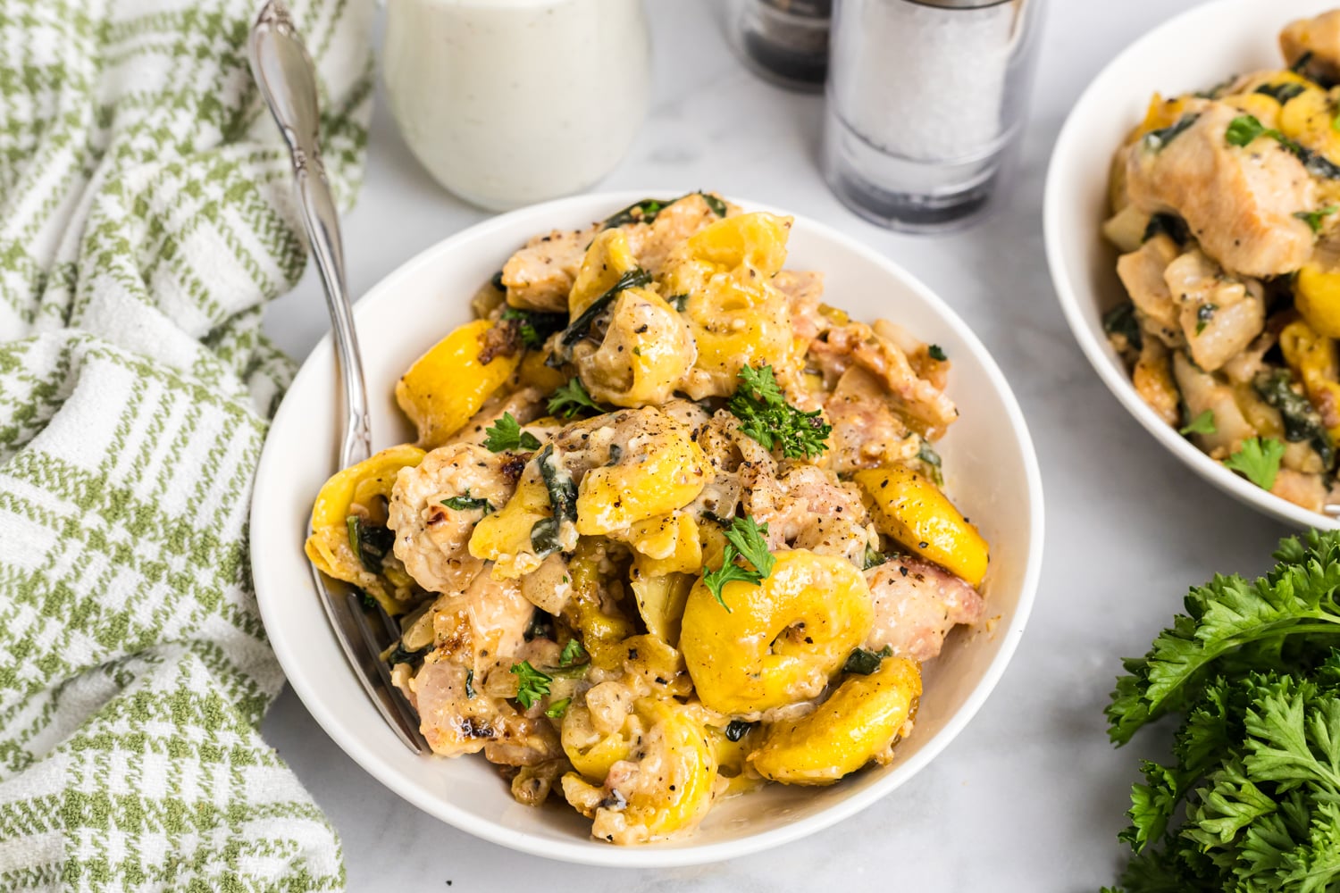 Bowl of creamy chicken bacon ranch tortellini topped with parsley and black pepper on a tabletop.