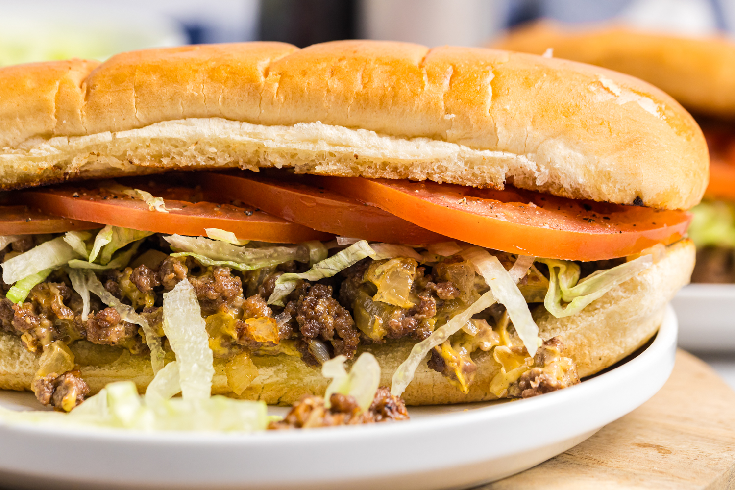 Close-up of a chopped cheese sandwich on a toasted hoagie roll filled with seasoned ground beef, melted cheese, shredded lettuce, and sliced tomatoes.