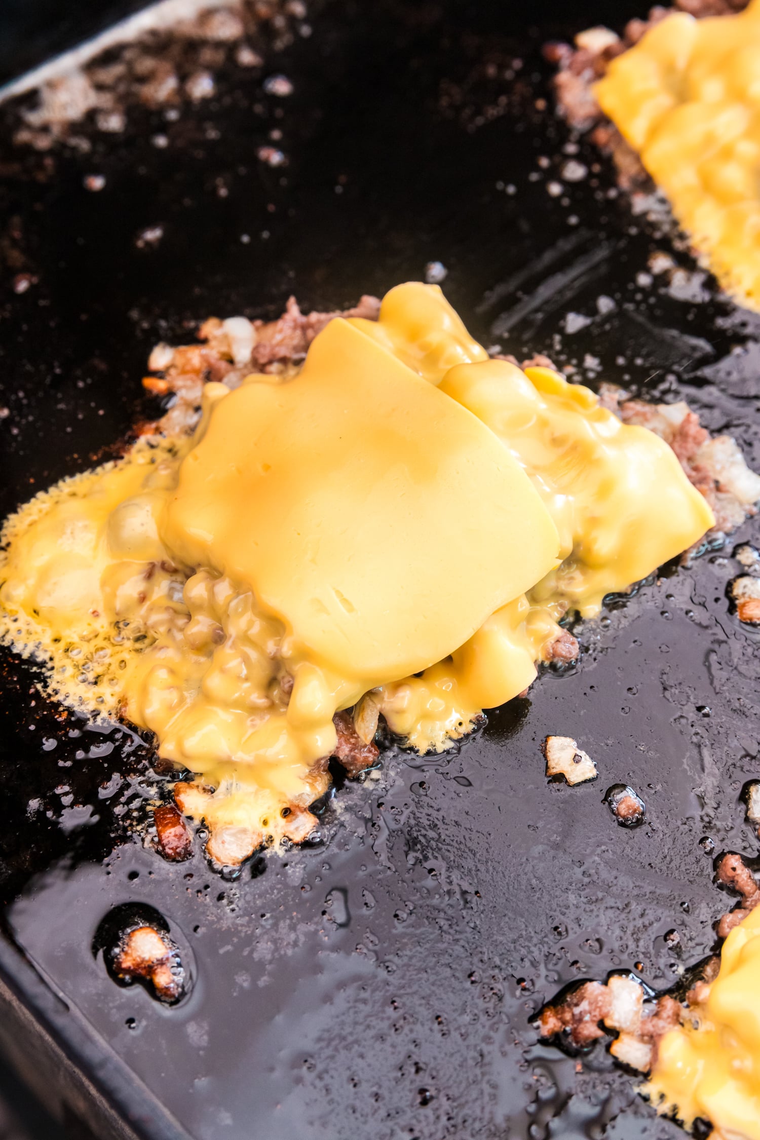 Chopped ground beef on a griddle topped with melting slices of American cheese.