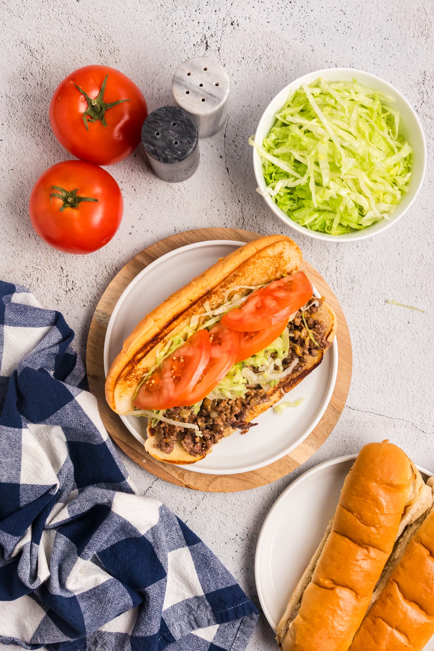 Overhead view of a chopped cheese sandwich on a toasted roll with ground beef, lettuce, and tomato, surrounded by fresh ingredients.