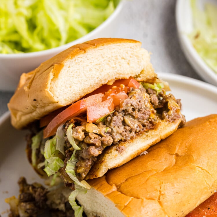 Halved chopped cheese sandwich showing the filling of seasoned beef, melted cheese, shredded lettuce, and tomatoes inside a toasted roll.