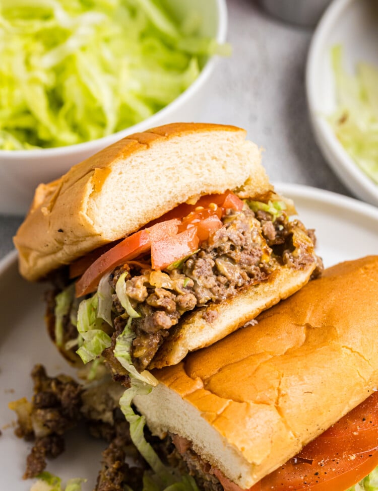 Halved chopped cheese sandwich showing the filling of seasoned beef, melted cheese, shredded lettuce, and tomatoes inside a toasted roll.