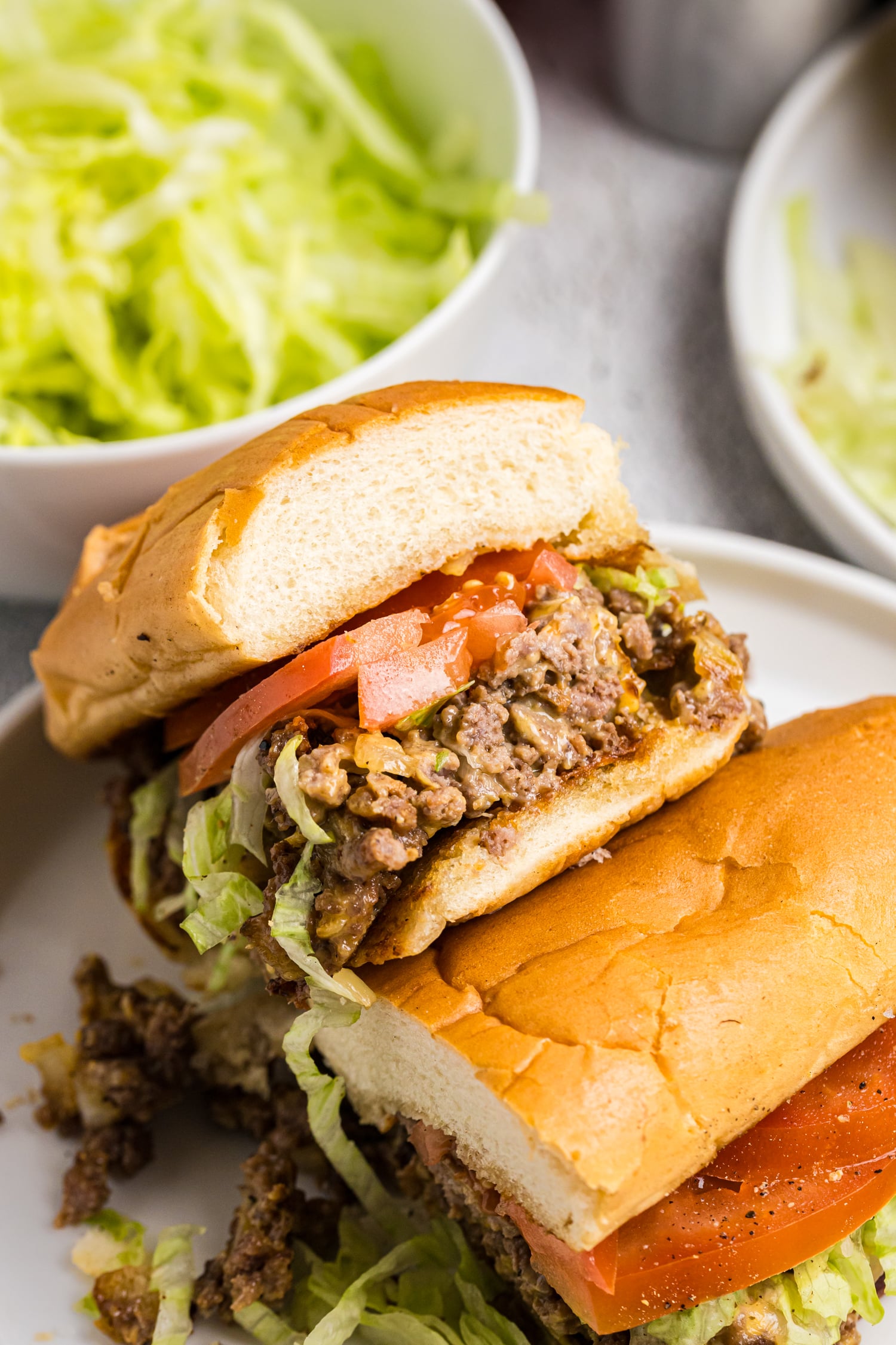Halved chopped cheese sandwich showing the filling of seasoned beef, melted cheese, shredded lettuce, and tomatoes inside a toasted roll.